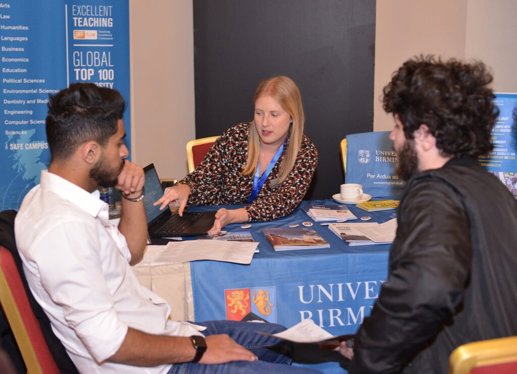A student in conversation with university representatives beside their banner