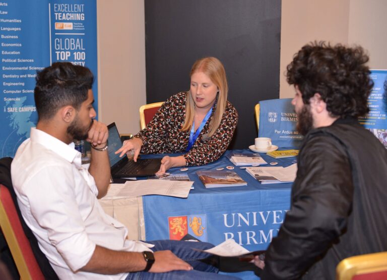 A student in conversation with university representatives beside their banner